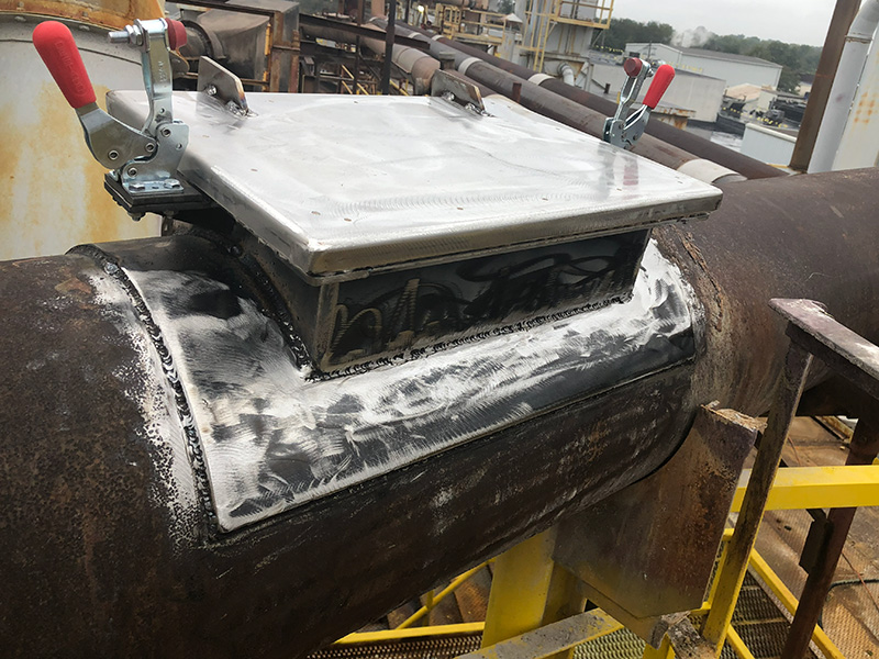 A newly fabricated access panel with latches attached to a large old pipe