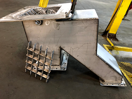 irregular shaped feed chute with grates inside the entrance opening at the top; there are two rectangular exits at the bottom