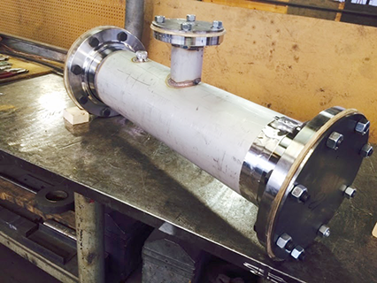 cylindrical oxygen line pipe fitting sitting on shop table, ends are capped closed for shipping
